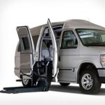 A silver van with its side doors open, featuring a deployed wheelchair lift, designed for accessible transportation.