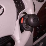 A close-up of a car’s steering wheel with a black and red spinner knob attached, designed to help make steering easier. Dashboard features and controls are partially visible in the background.