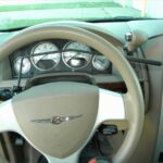 A car steering wheel with hand controls installed for accessibility, showing dashboard gauges and a beige interior.