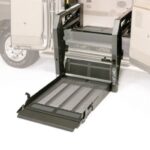 A wheelchair lift is extended from the side of a van, providing accessible entry. The lift platform is lowered to the ground, with the van door open in the background.