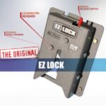 EZ Lock device with labeled parts: locking pin receiver, manual release switch, and durable steel housing. Text reads THE ORIGINAL EZ LOCK and Made in USA. The device is mounted on a metal plate.