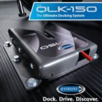 A close-up of the QLK-150 docking system by Q’STRAINT, mounted on a grooved surface, with bold text reading The Ultimate Docking System and Dock. Drive. Discover. in the image corners.