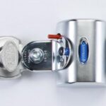 Close-up of a silver combination padlock securing a latch with a black strap. The padlock has a circular key mechanism and a red tab, with a blue logo that reads Gusset Guard.