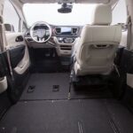 Interior view of a wheelchair-accessible van, showing lowered floor, spacious open area, and front driver and passenger seats with beige upholstery. Steering wheel and dashboard are visible.
