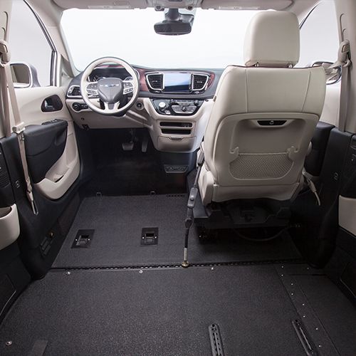 Interior view of a wheelchair-accessible van, showing lowered floor, spacious open area, and front driver and passenger seats with beige upholstery. Steering wheel and dashboard are visible.