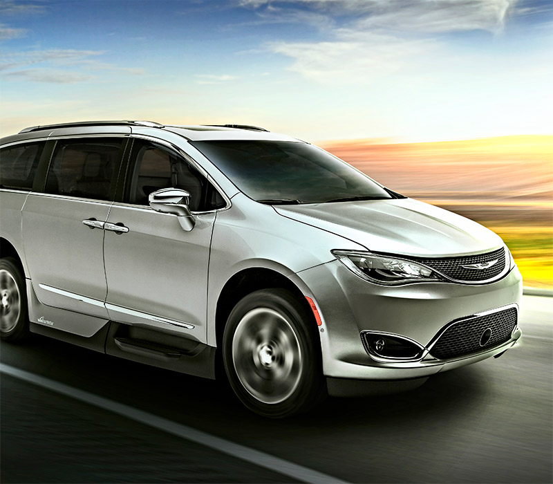 A silver minivan driving on a highway with a blurred background of fields and a blue sky, suggesting motion and speed.