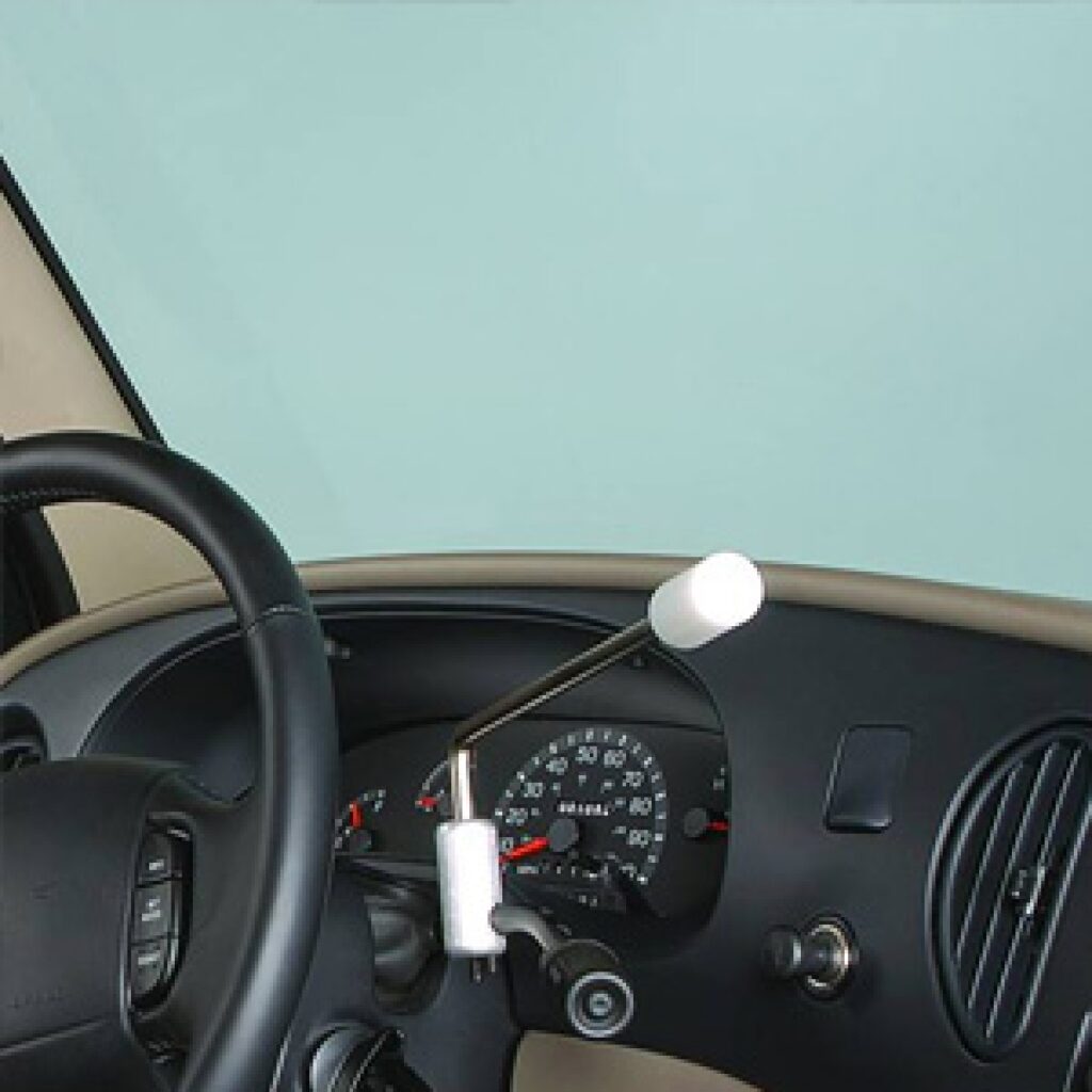 Close-up of a car dashboard with a hand control device attached to the steering column, designed to help people with physical disabilities operate the vehicle. The speedometer and air vent are also visible.