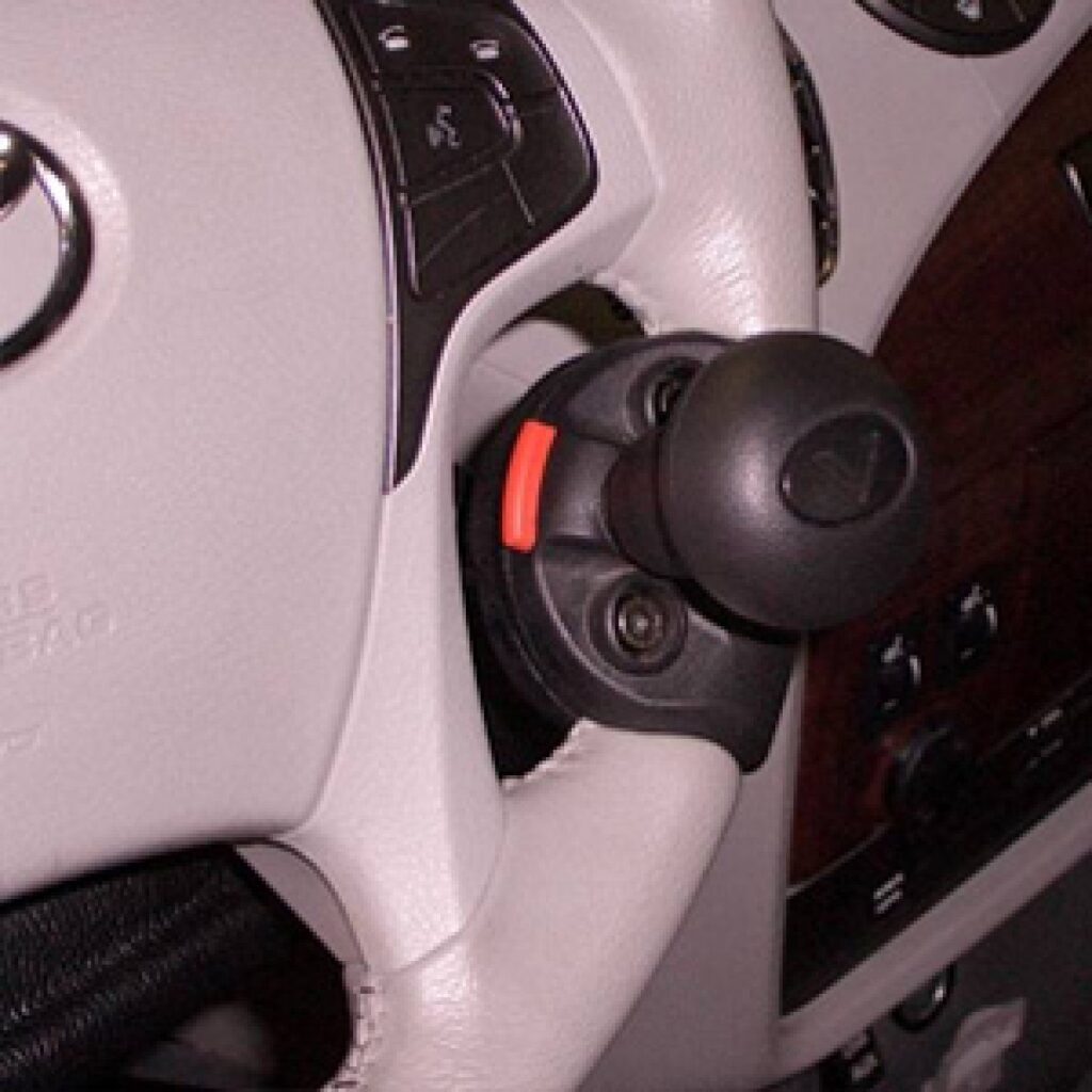A close-up of a car’s steering wheel with a black and red spinner knob attached, designed to help make steering easier. Dashboard features and controls are partially visible in the background.