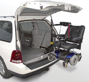 A van with its rear hatch open uses a mechanical lift to load an electric wheelchair into the back of the vehicle.