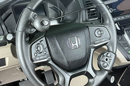 Close-up of a Honda car steering wheel equipped with various adaptive driving controls and buttons, designed for accessibility to assist drivers with limited hand mobility.
