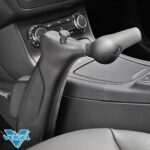 A close-up view of a cars interior showing a Veigel-brand hand control device for driving, positioned next to the drivers seat near the center console and dashboard controls.