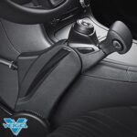 Close-up of a black mechanical hand control device installed next to the driver’s seat in a car, used for assisting drivers with limited mobility. The Veigel logo is visible in the bottom left corner.