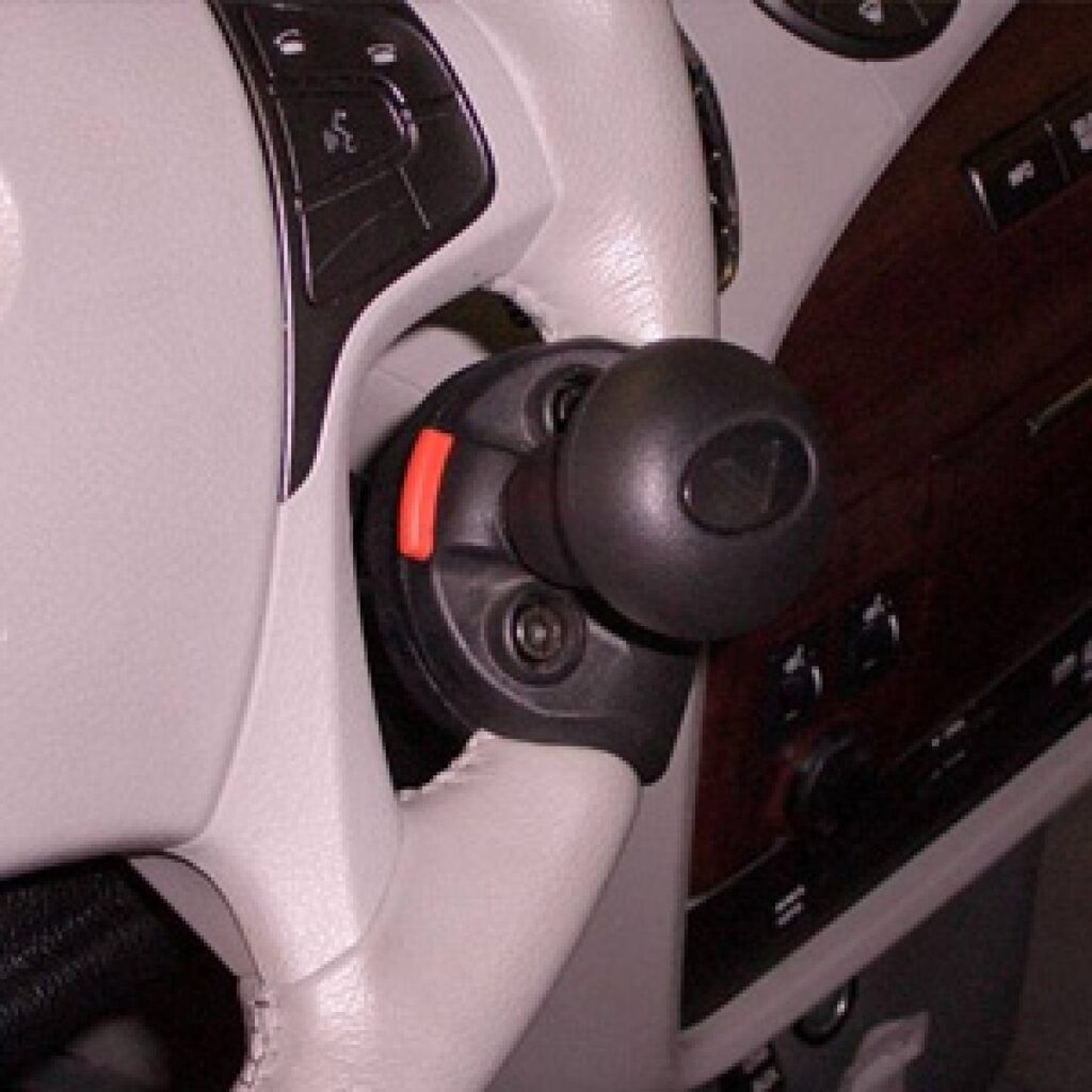 A close-up of a cars steering wheel with a black steering knob attached, designed to assist with one-handed steering. The interior features light-colored leather and wood trim.