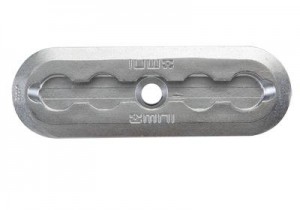 Rectangular metal connector plate with rounded ends, a central circular hole, and four smaller oval slots arranged in pairs on each side. The plate has embossed markings and a grooved surface.