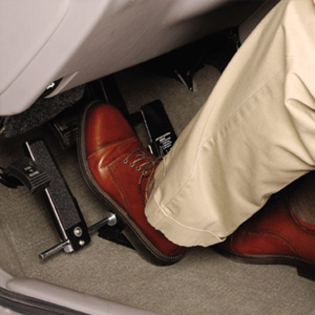 A person wearing tan pants and brown leather shoes is pressing the accelerator pedal in a car, with their foot on the pedal and the other foot nearby on the floor mat.