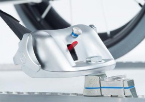 Close-up of a metallic bike lock mechanism securing a bicycle wheel, with a thick silver chain and locking bolts visible on a white background.