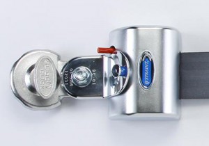 Close-up of a silver security lock with a round keyhole and a blue GUARDIAN label, attached to a black strap. A red lever or switch is visible on the top of the lock.